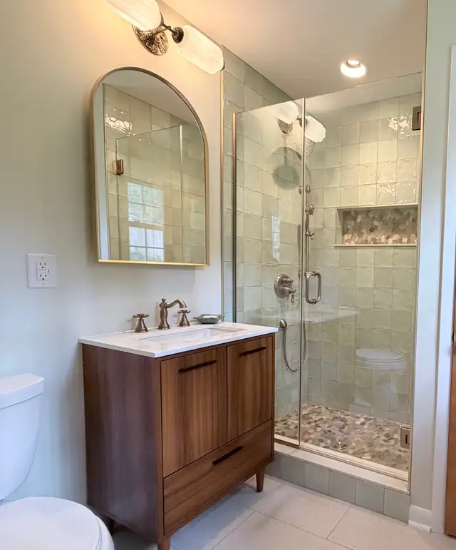 Raleigh primary bathroom with soft green shower tile, pebble-stone shower floor and niche, frameless glass and a wood vanity