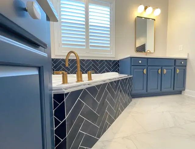 Bathroom with navy herringbone tile tub skirt, blue vanity with brass hardware and marble-look floor