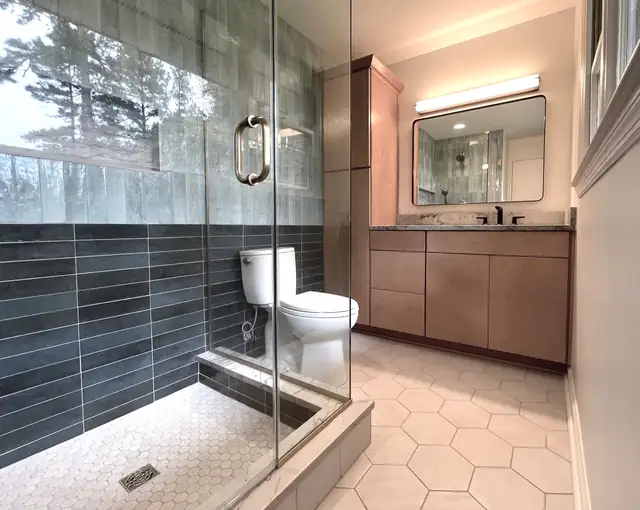 Bathroom with a glass shower, blue-green and slate wall tile, hexagon floor tile and a wood vanity