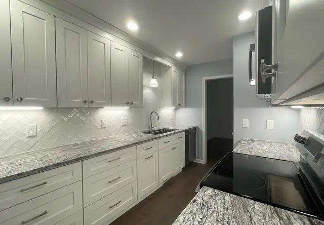 Galley kitchen remodel in Raleigh, NC with white cabinets, herringbone subway backsplash and Blue Dunes granite